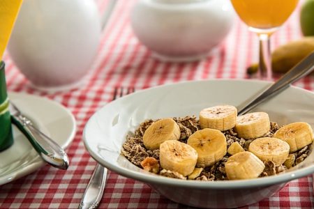A healthy breakfast bowl with sliced bananas and cereal on a red checkered tablecloth.
